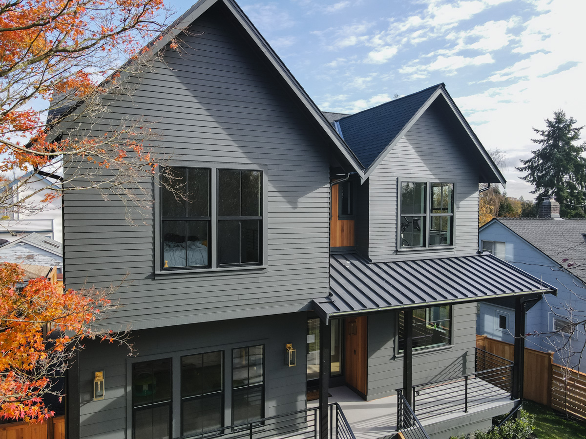 Front elevation with vibrant autumn foliage showing charcoal architectural shingles, gabled rooflines, and standing seam metal porch roof