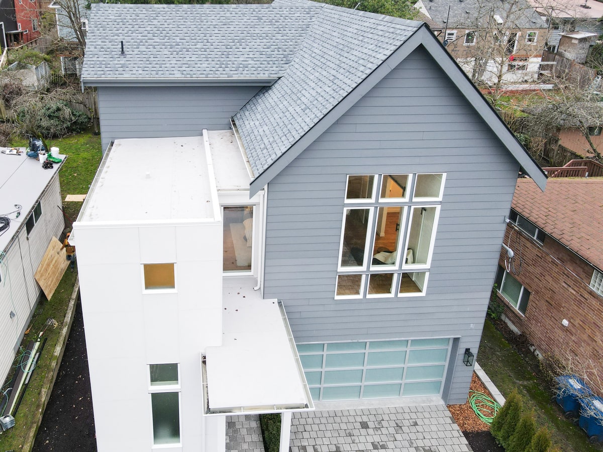 High-angle aerial view of architectural shingle gables, muted blue lap siding, and white panel tower on Seattle WA home