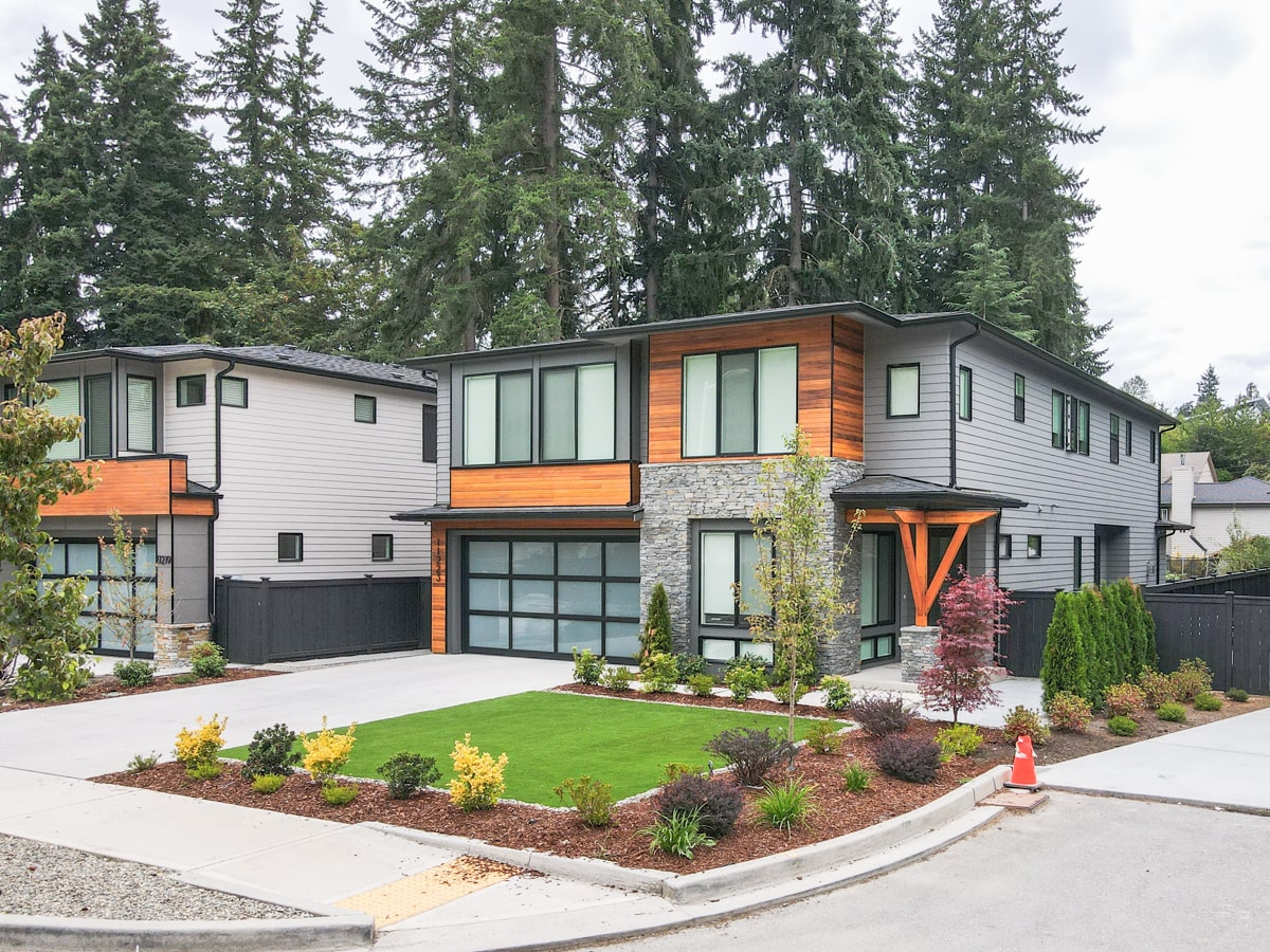 Street-level view of new construction modern home with cedar siding, stone facade, and architectural shingle roof
