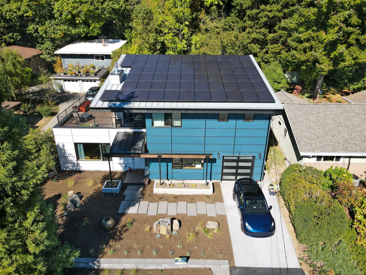 Elevated front drone view of completed modern rebuild, showing landscape pavers, modern siding, and full rooftop solar array
