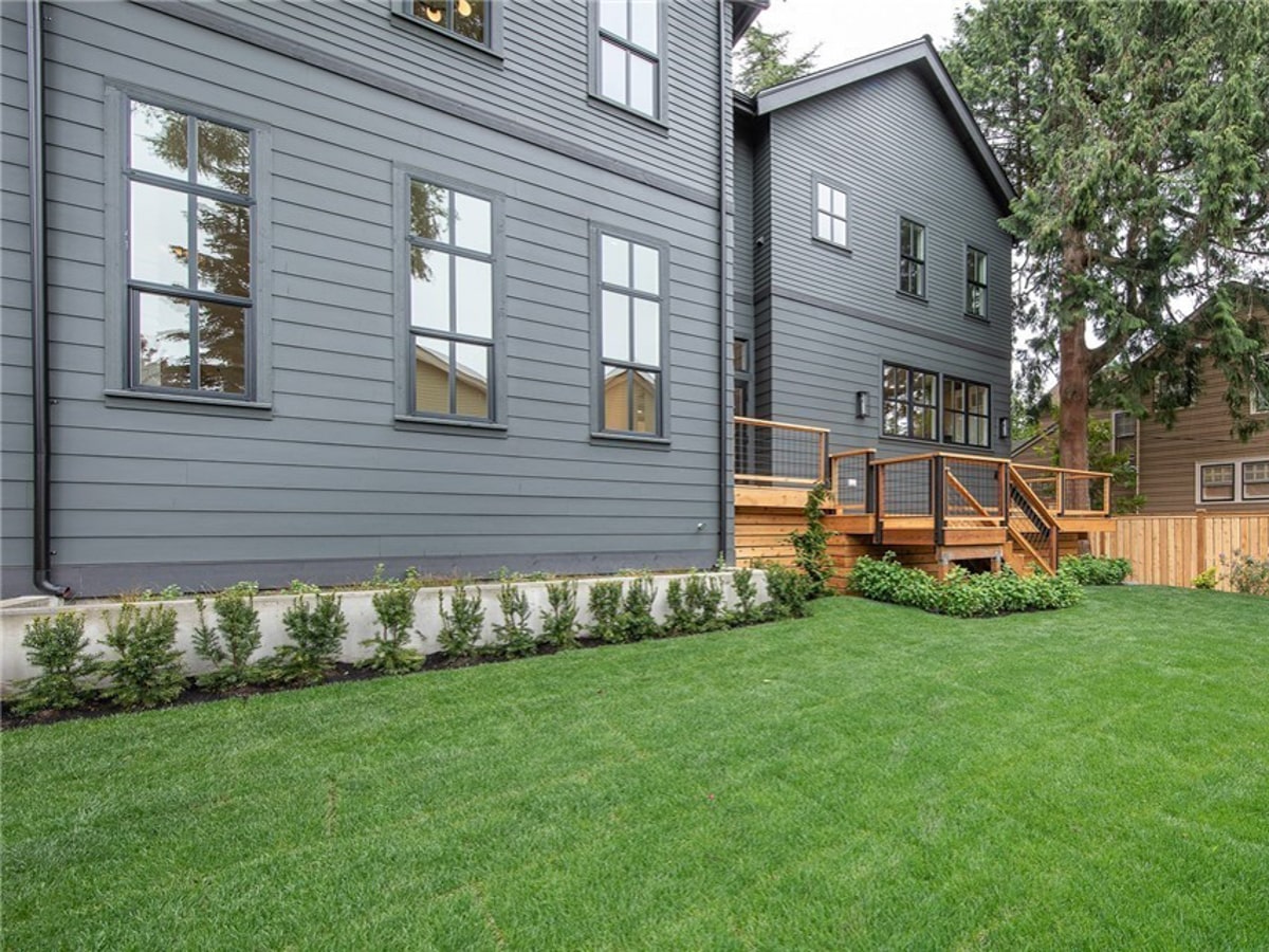 Side exterior view highlighting clean charcoal lap siding, black-trimmed windows, concrete retaining border, and custom wood deck