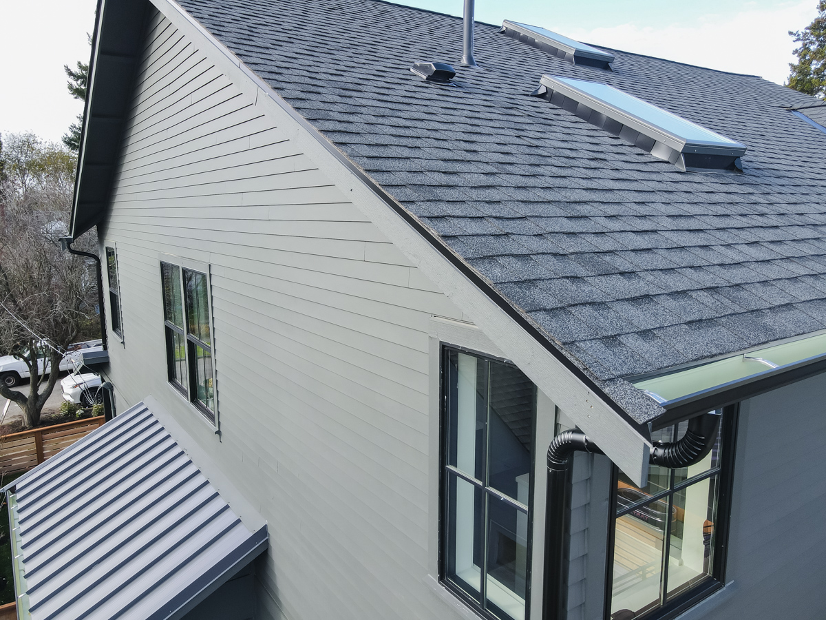 Close-up detail of roof rake edge, gutter system, dual skylights, and standing seam awning metalwork