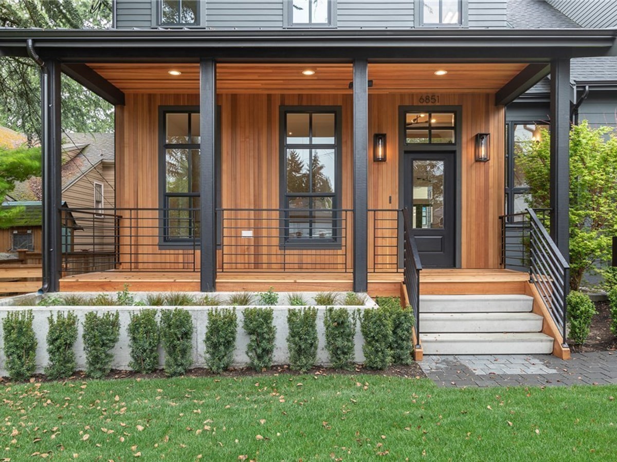 Architectural front porch detail with warm natural wood wall and ceiling paneling, modern black metal railings, and concrete planter
