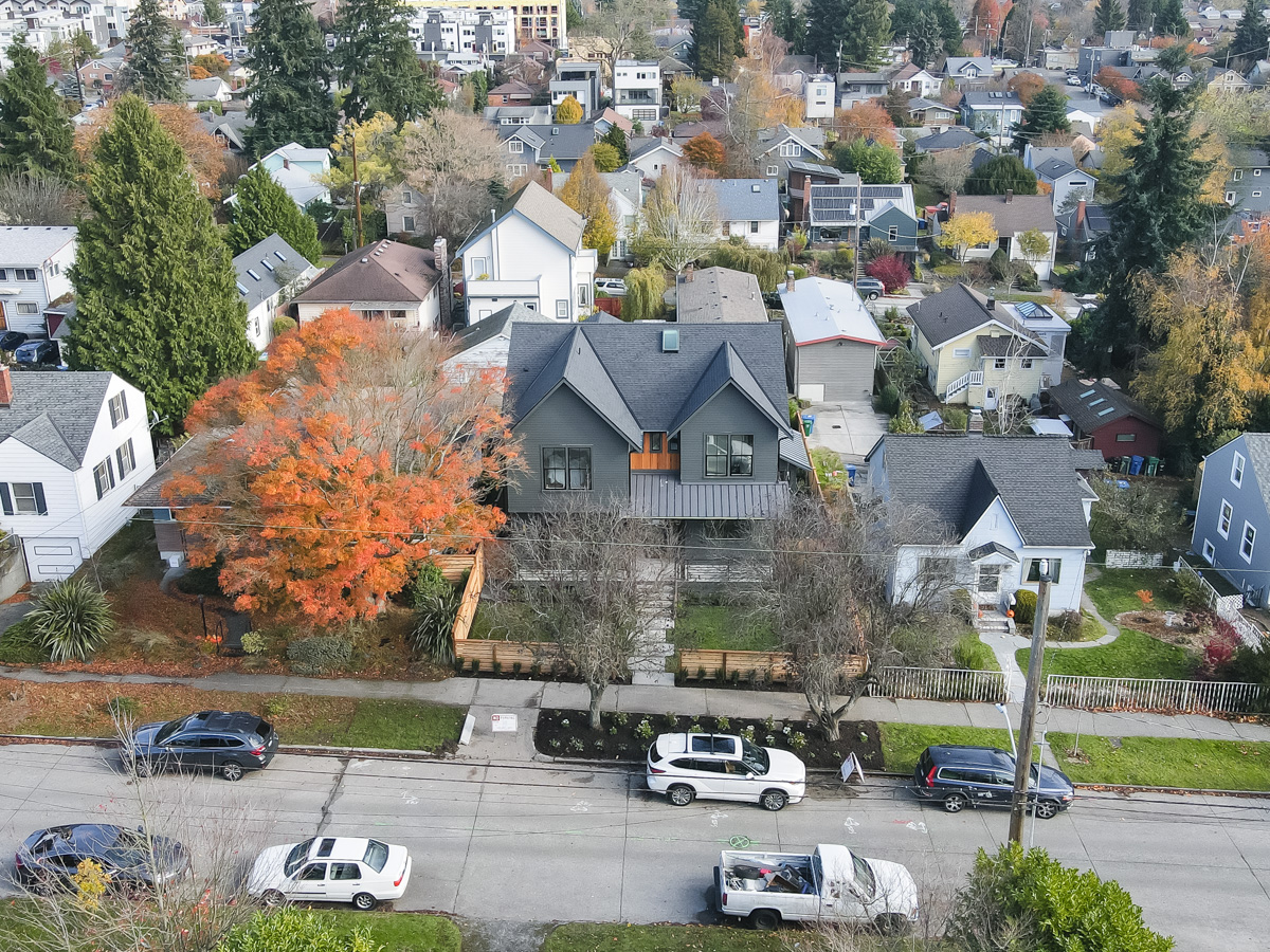 High-angle neighborhood aerial overview of charcoal dual gabled roof, standing seam porch roof, and surrounding Seattle streetscape