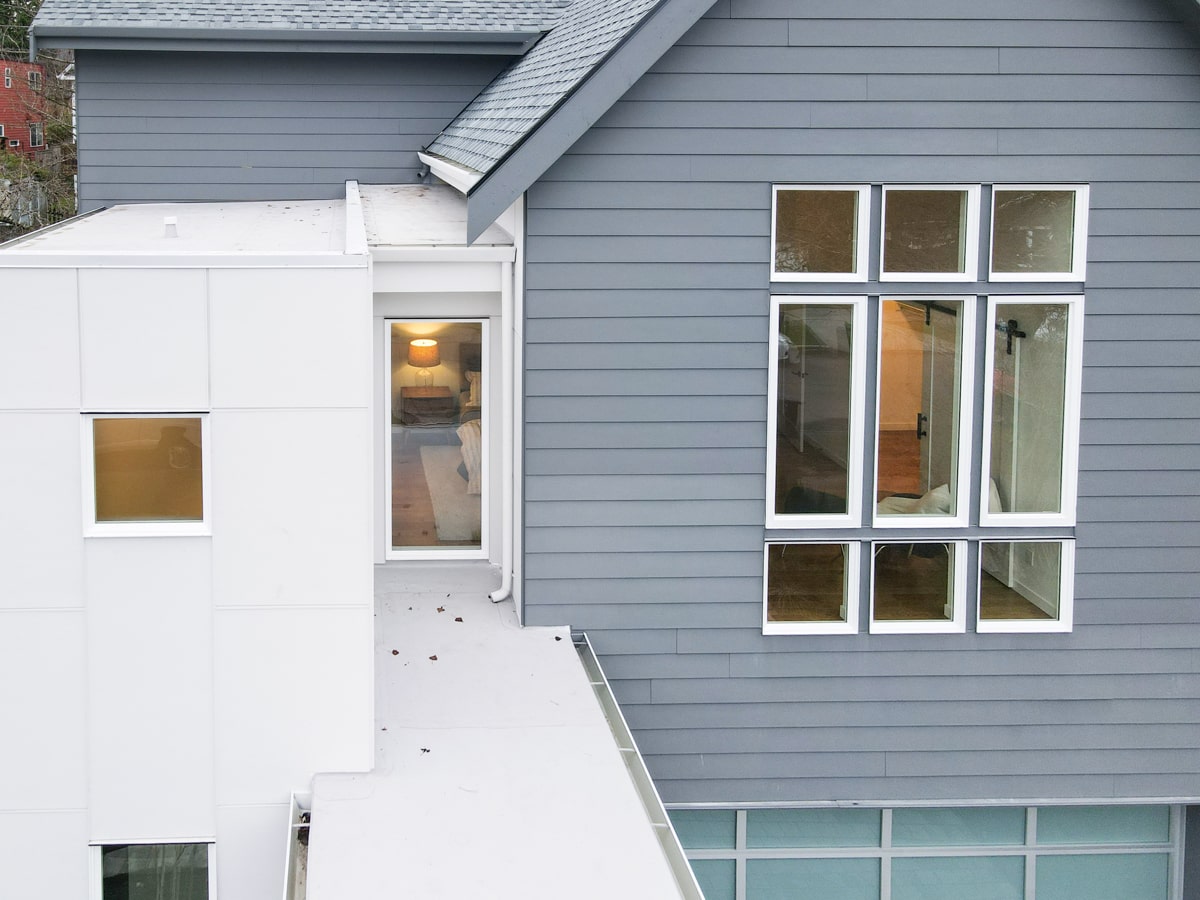 Upper facade close-up showing custom window grid, muted blue Hardie lap siding, and roof overhang