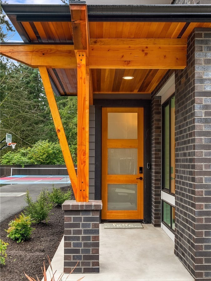 Covered timber porch entry with cedar ceiling paneling, brick pedestal pillar, and custom wood front door