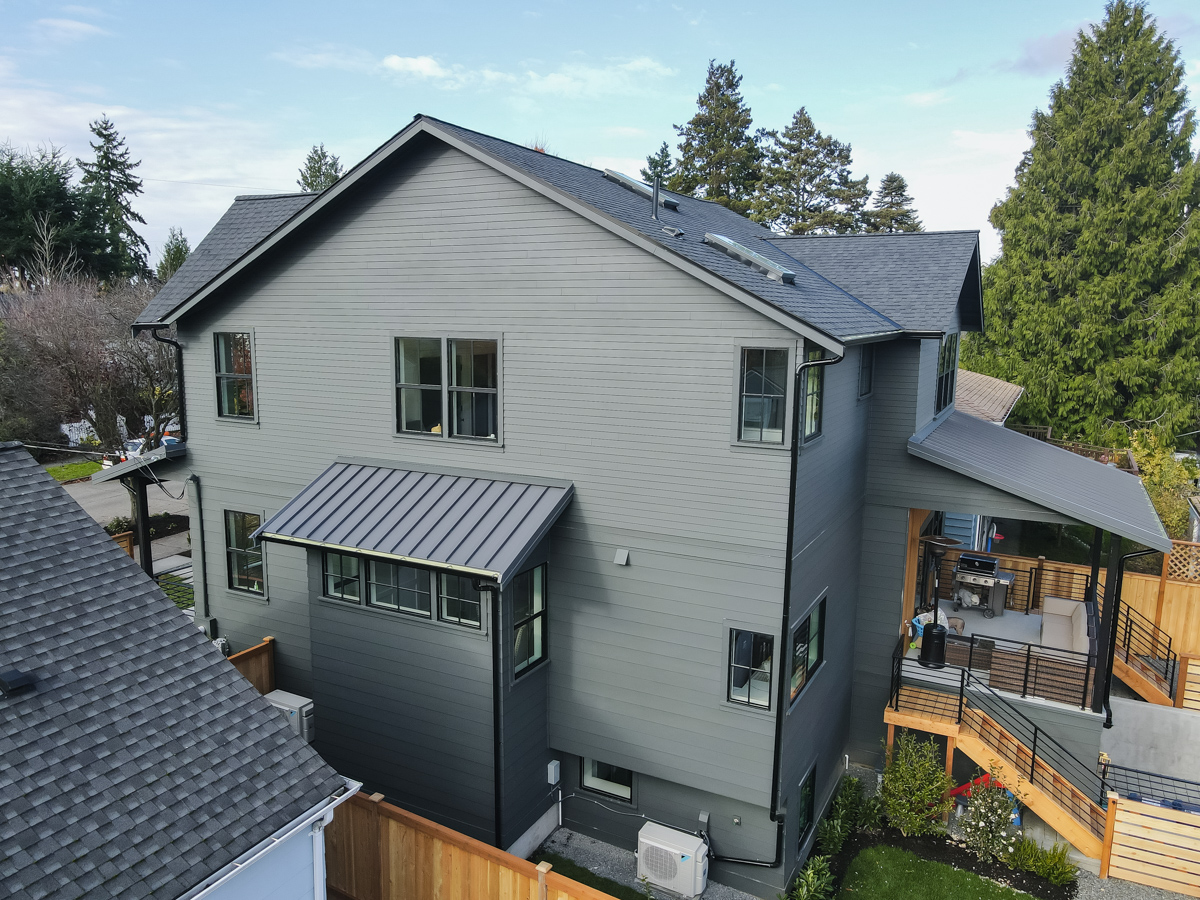 Side exterior view showcasing metal window awning, charcoal architectural shingles, downspouts, and cedar privacy fence