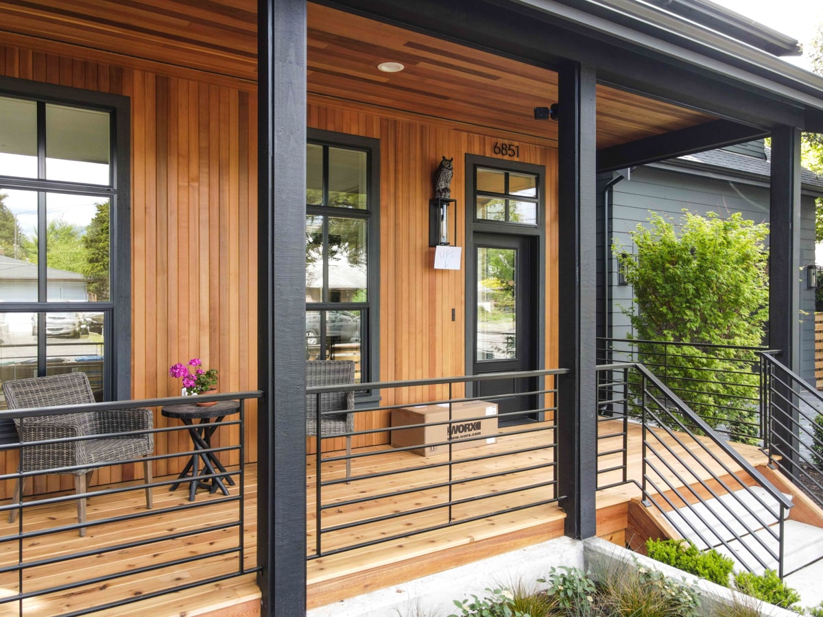 Front porch detail featuring natural pine wood wall paneling, cedar wood decking, and black steel railings
