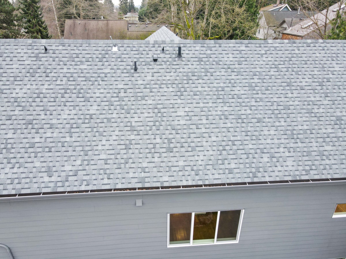 Detailed aerial view of light gray architectural shingle roof slope and clean gutter line