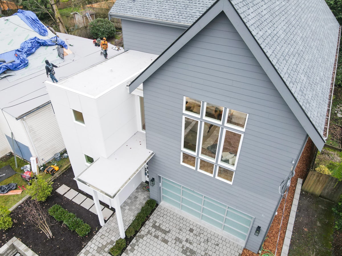 Elevated front view of muted blue Hardie siding gable, white panel tower, paver driveway, and architectural shingle roof