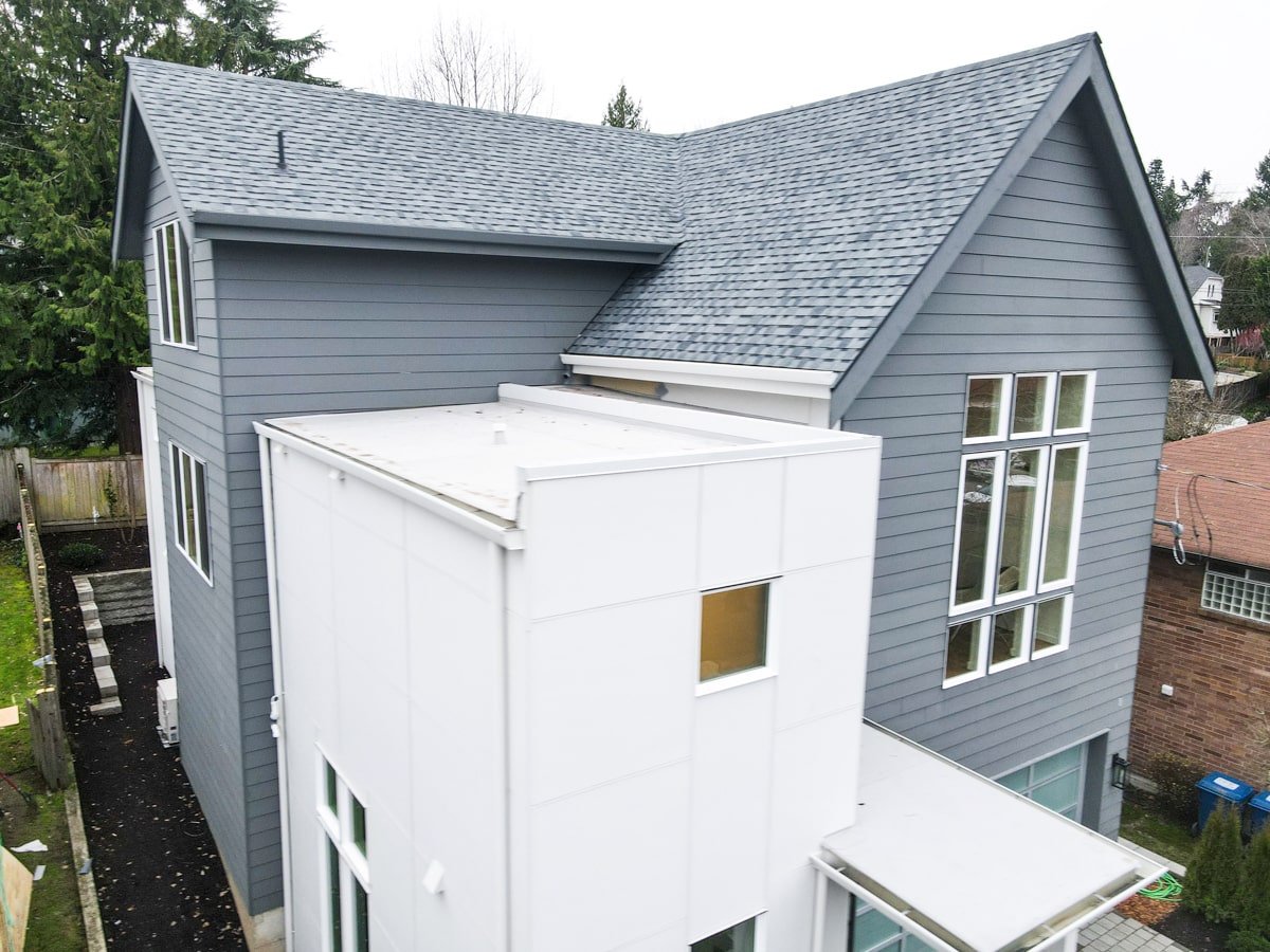 Three-quarter aerial view of complete architectural shingle roof installation, ridge lines, and modern siding in Seattle WA