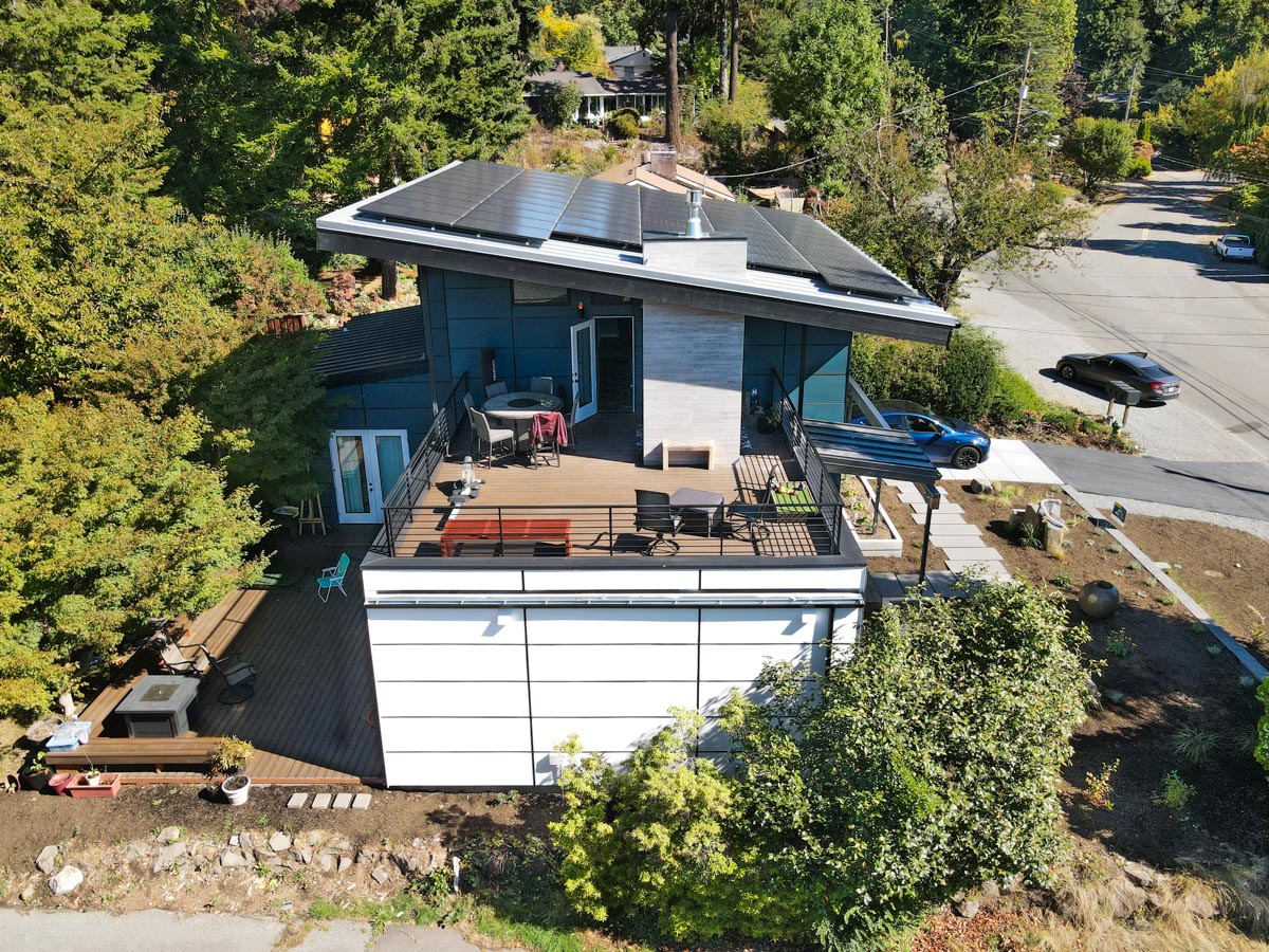 High-angle drone view of rear multi-level outdoor living deck, modern chimney, and solar roof installation