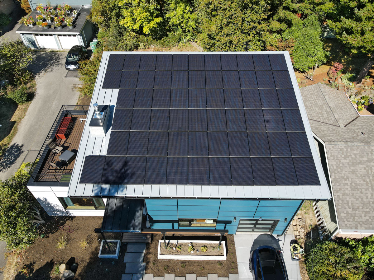 Direct top-down drone photograph of the full rooftop solar array, Kebony natural wood deck, and modern metal fascia