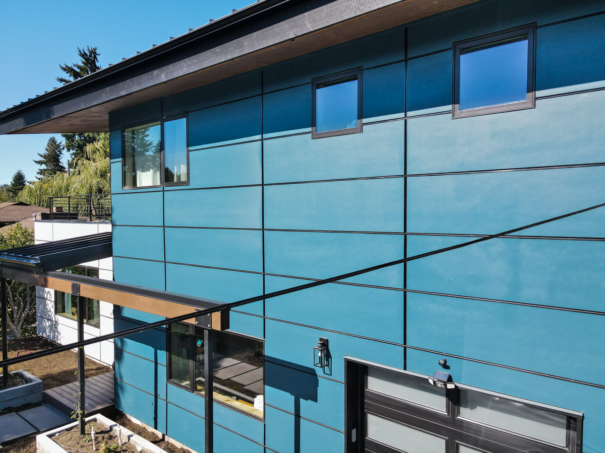 Detailed architectural angle of smoky blue siding panels, dark metal fascia, and upper story windows under clear blue sky