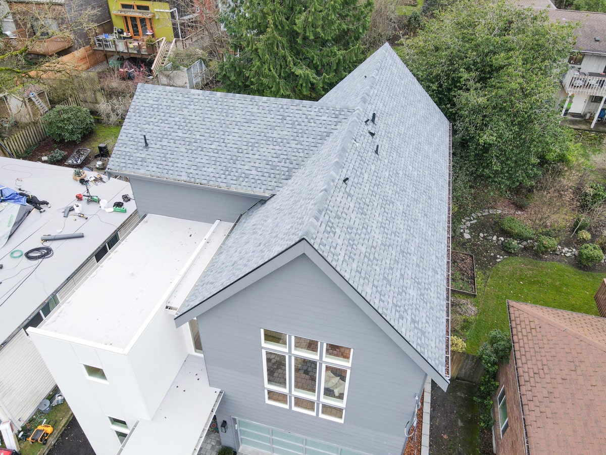 Overhead aerial view of steep architectural shingle rooflines, valleys, and muted blue siding gable in Seattle WA