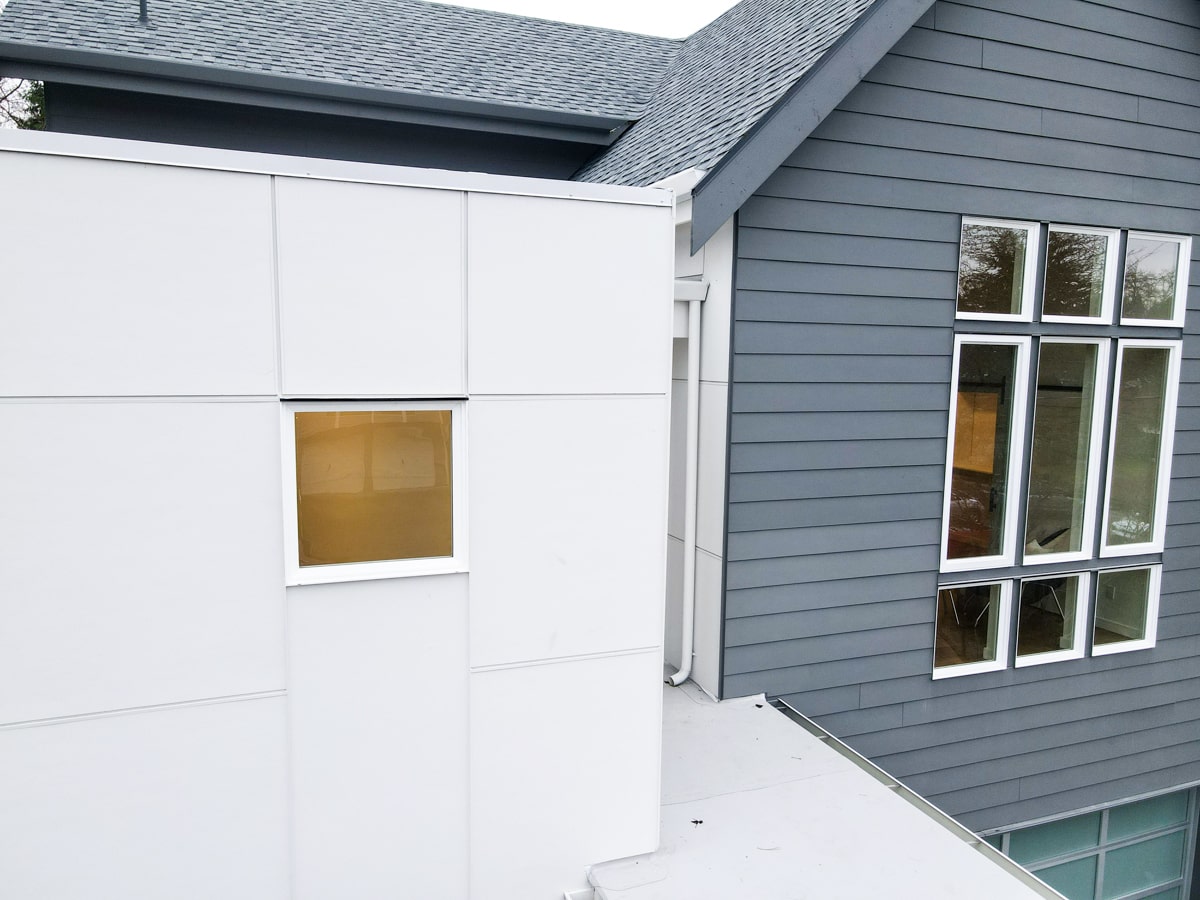 Exterior junction detail showing clean white panel siding, trim lines, and architectural shingle roof eave