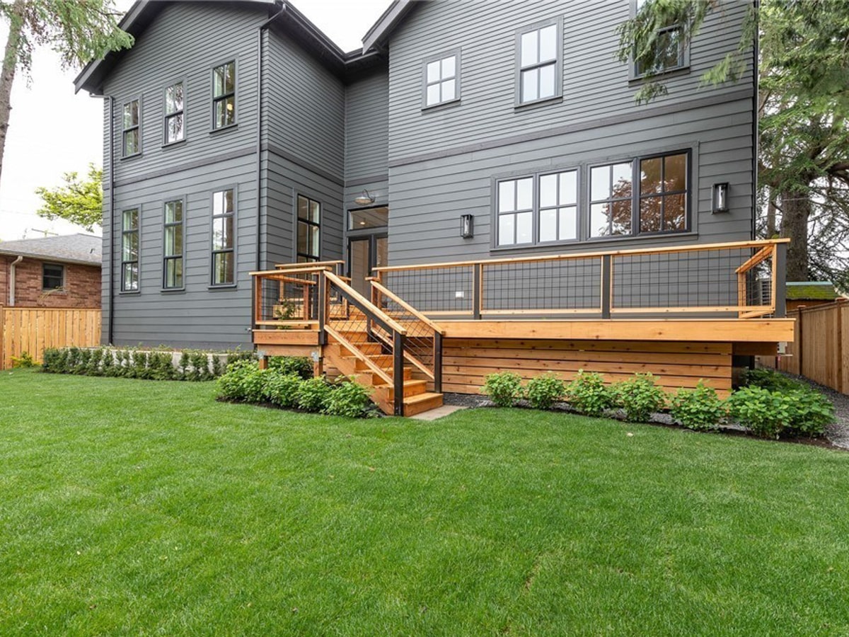 Spacious backyard featuring custom cedar entertaining deck with modern wire railings, staircase, and manicured green lawn