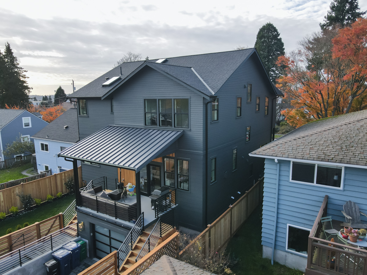 Rear exterior elevation showing elevated covered deck with standing seam metal roofing, glass garage door, and modern staircase