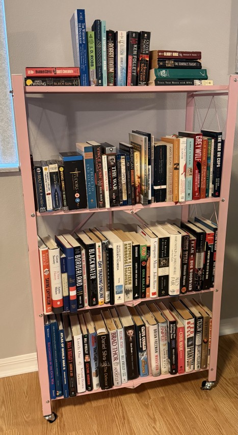 Pink metal folding bookshelf on caster wheels filled with organized books