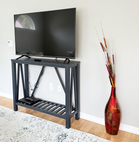 Flat screen TV on dark wood trestle console table with tall red floor vase