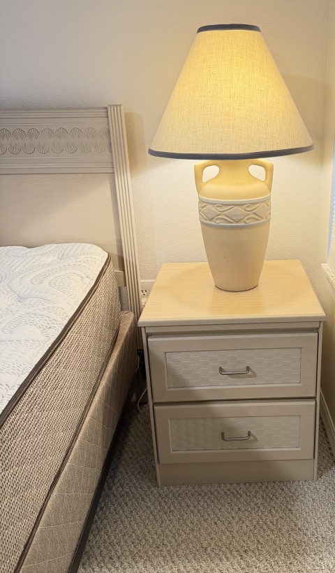 Cream two-drawer nightstand with ceramic urn table lamp and headboard detail