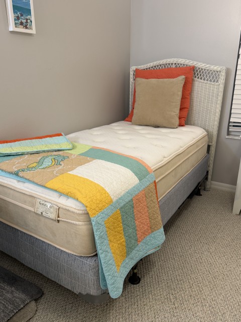 Twin bed with white wicker headboard, coastal quilt, and pillows