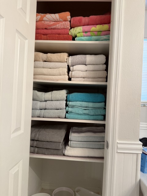 Linen closet shelves organized with neatly folded colorful bath and hand towels