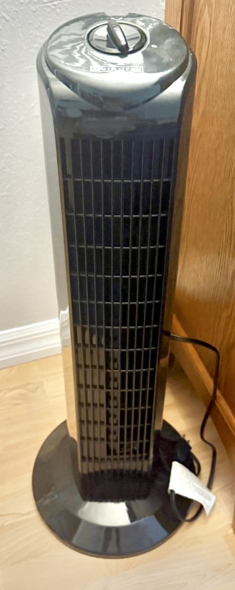 Black oscillating electric tower fan on round floor base