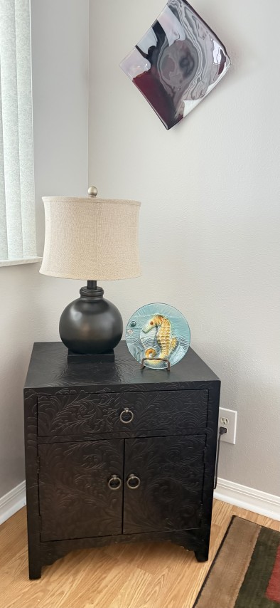 Black carved wood nightstand cabinet with dark globe lamp and decorative seahorse glass accent