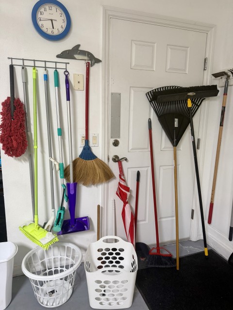 Garage cleaning organization with brooms, mops, rakes, wall clock, and laundry hampers