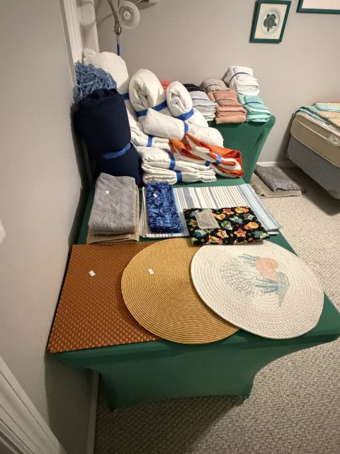 Folded bed linens, blankets, and round woven placemats on display table