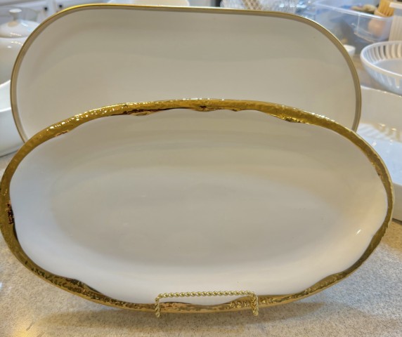 White ceramic oval serving platters with hammered gold rim on display stand