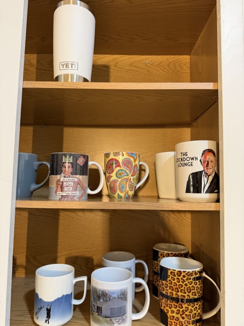 Cabinet shelves displaying novelty coffee mugs, graphic mugs, and Yeti tumbler