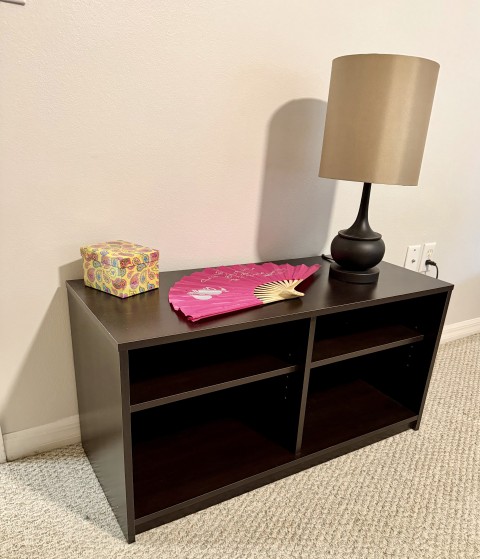 Dark brown low storage shelf with table lamp, gift box, and decorative pink folding fan