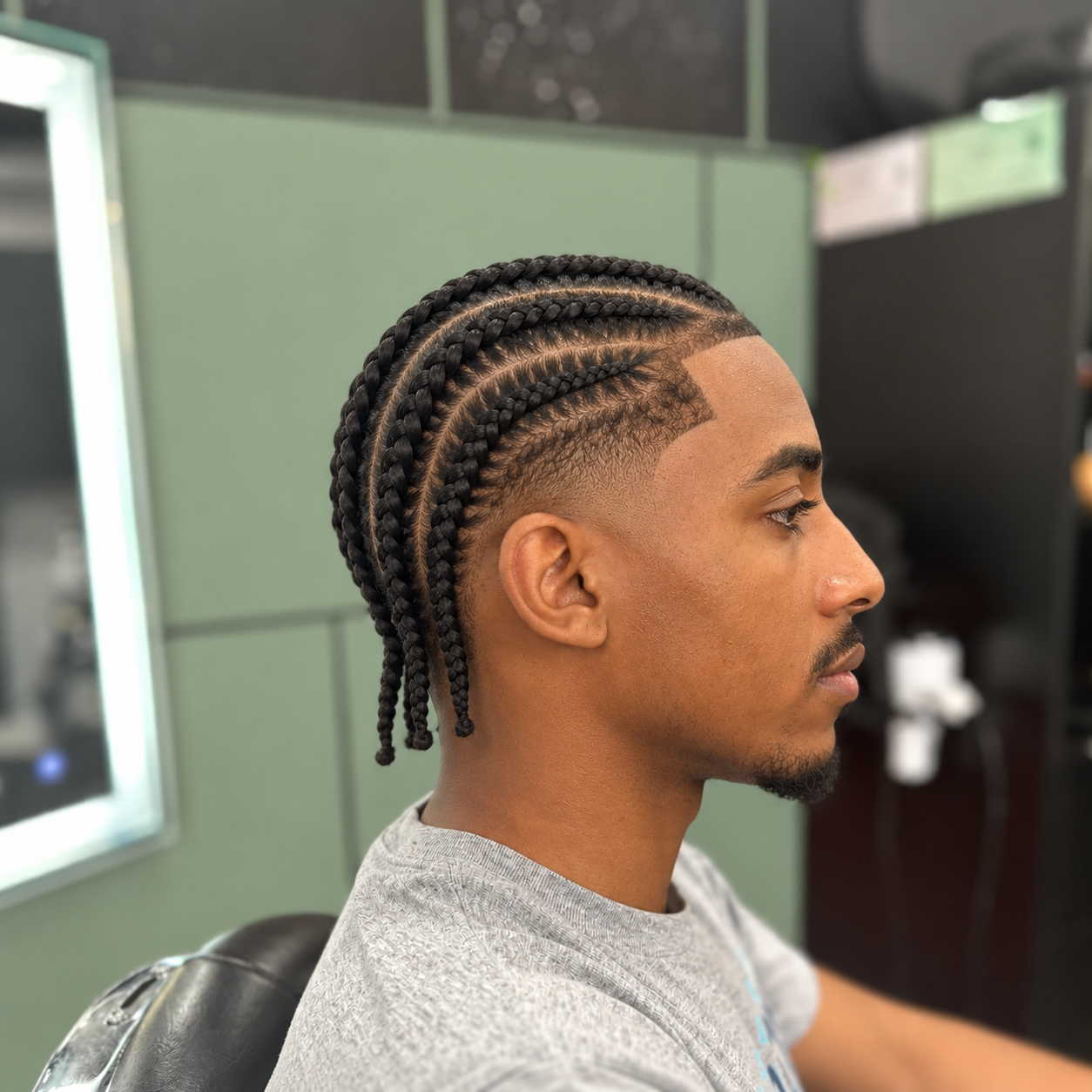 A man with clean precision cornrow braids and a sharp hairline styled at MANE DISTRICT