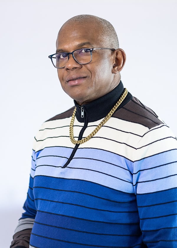 Portrait of a man in glasses, a gold chain, and a striped blue sweater.