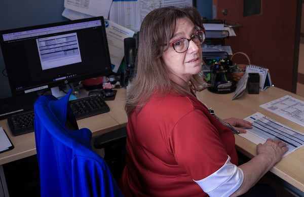 A woman in glasses and a red shirt reviews documents at her desk.