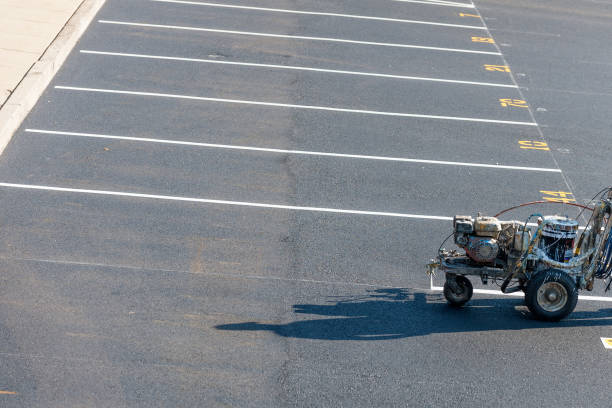 Professional line-striping machine laying clean white parking lines and yellow numbered stalls on dark asphalt