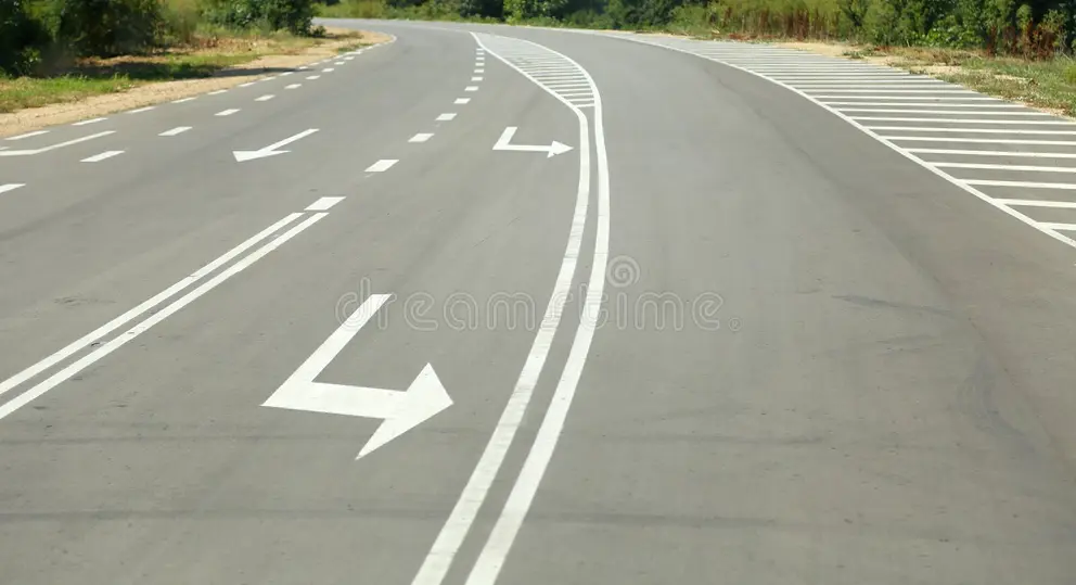 Crisp white directional traffic arrows and lane markings stenciled on freshly paved roadway asphalt