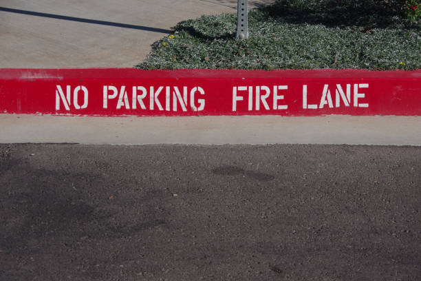 Bright red curb painted with bold white stenciled 'NO PARKING FIRE LANE' emergency marking