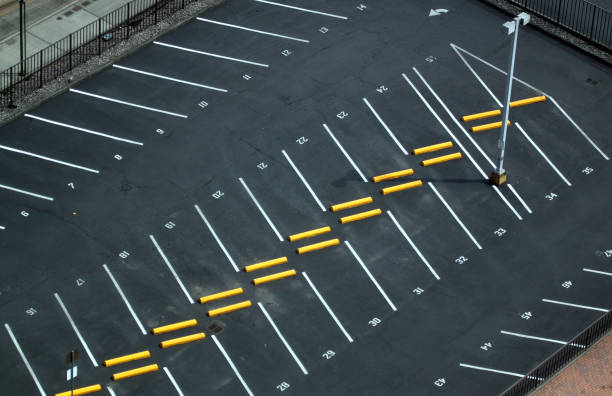 Aerial view of a freshly striped commercial parking lot with crisp white stalls, yellow wheel stops, and numbered spaces