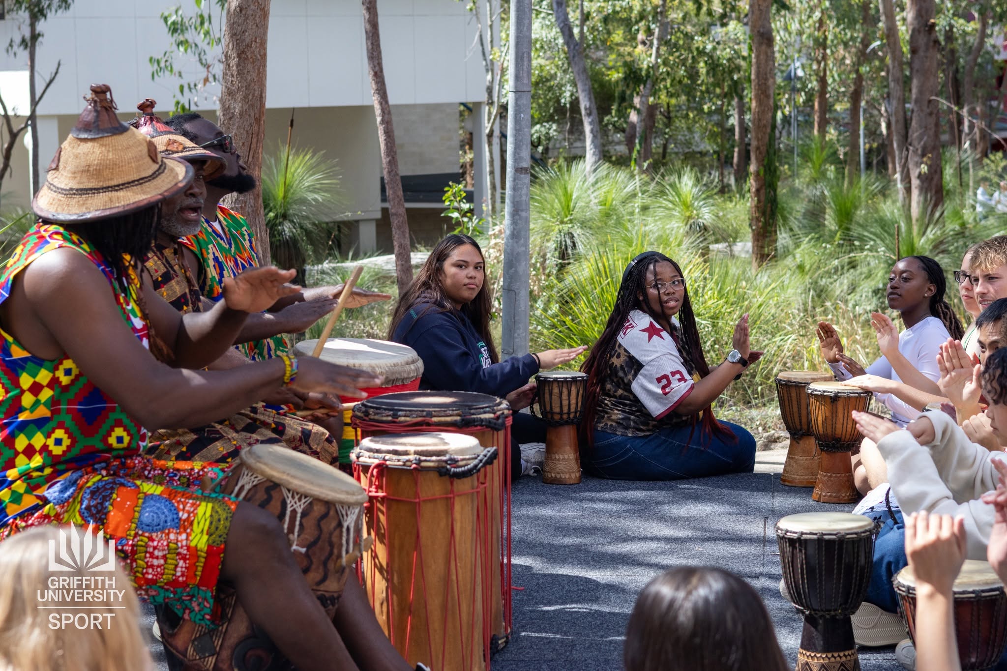 African Beat drummers and dancers performing in a leafy university campus courtyard with a seated student audience