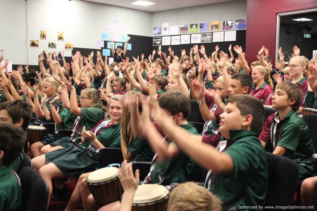School students enthusiastically raising their hands and cheering with djembe drums during an African Beat school assembly presentation