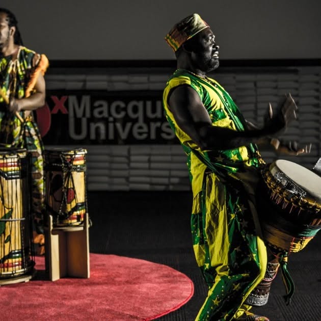 Macquarie University stage show featuring an African Beat dancer in green and yellow traditional dress performing live on stage