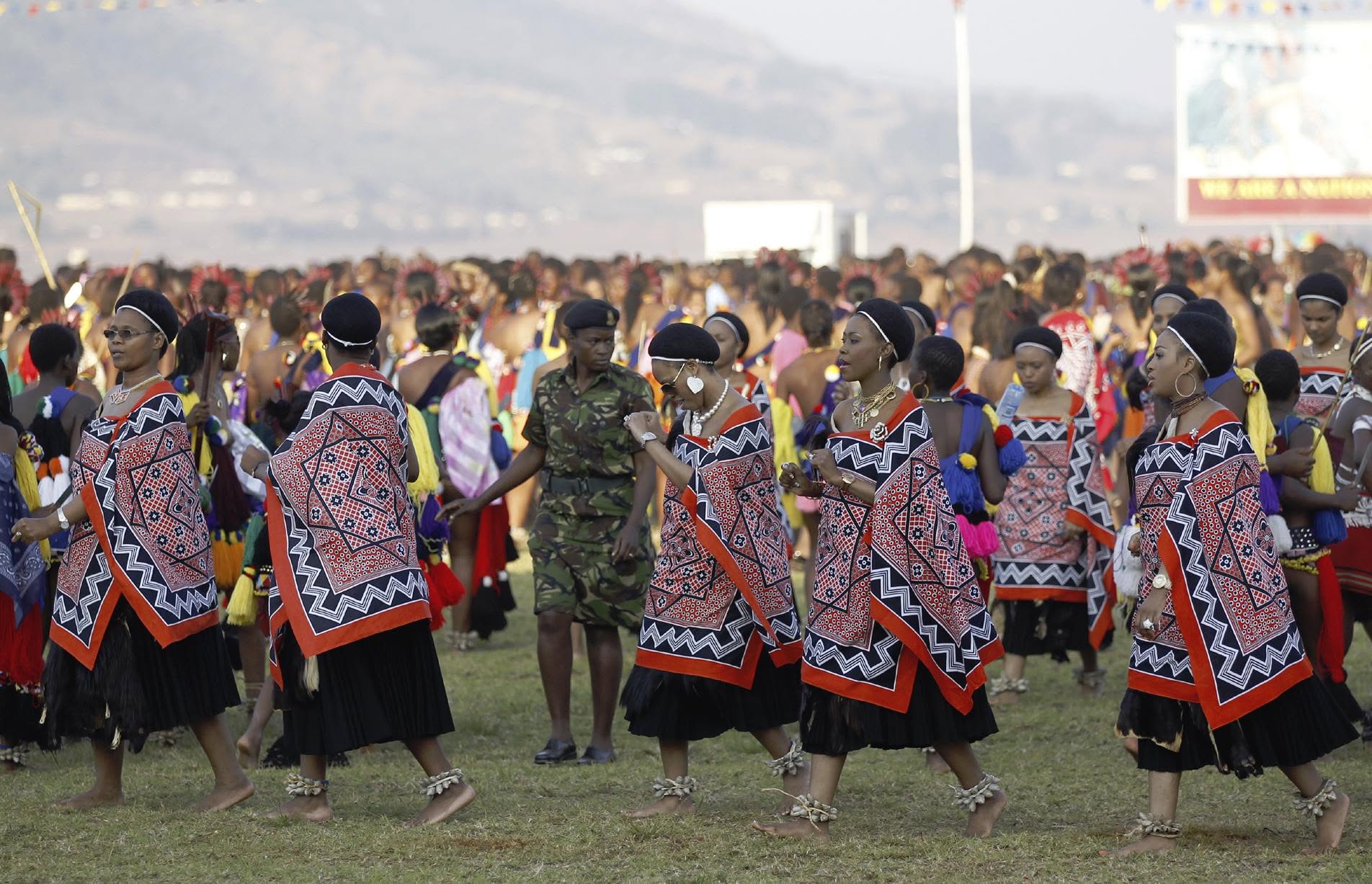 Dancers in traditional patterned attire processing proudly in front of a large festival crowd