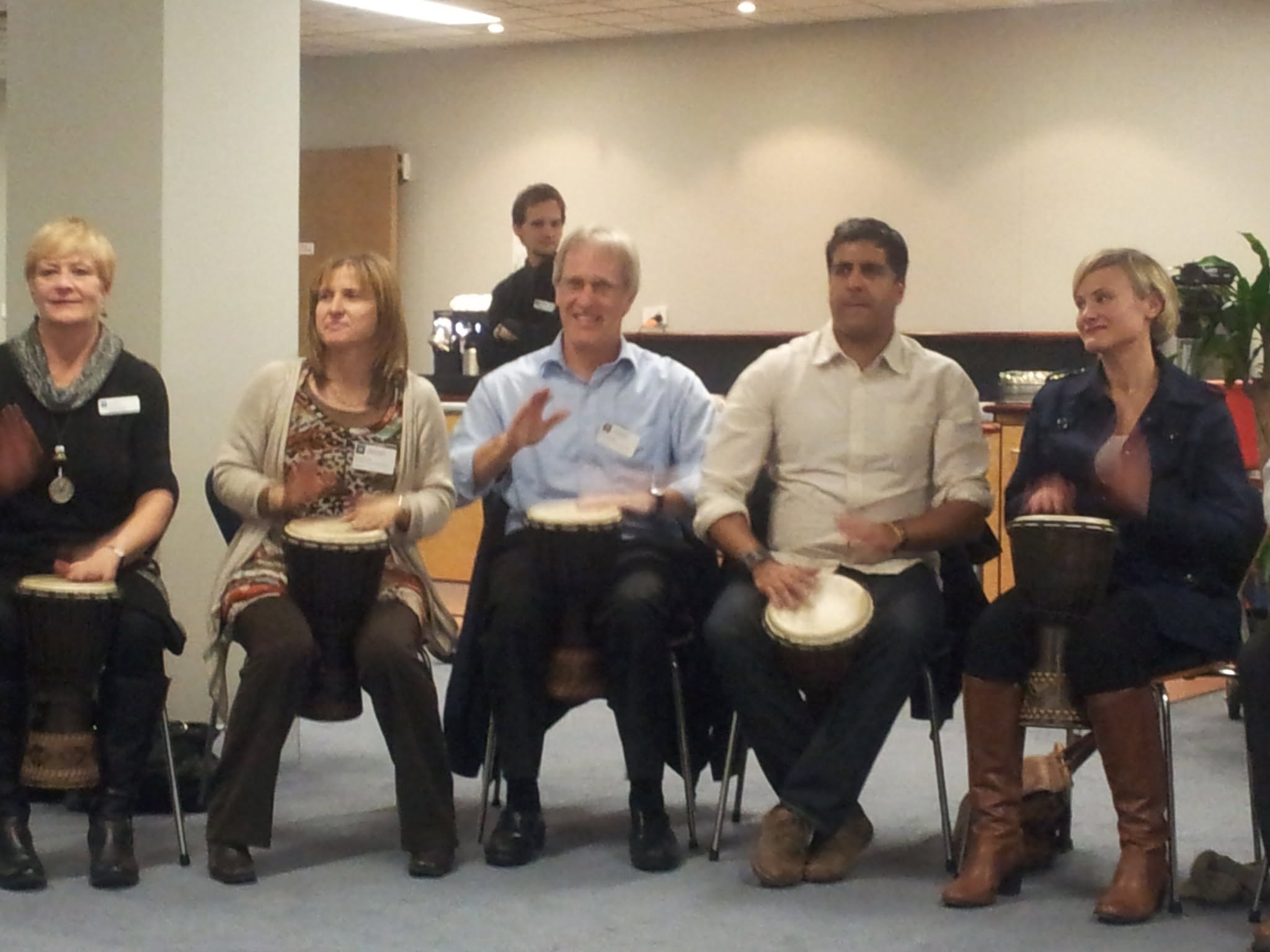 Corporate staff seated in a row playing djembe drums during an African Beat wellbeing workshop