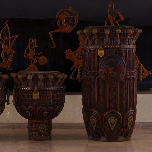Close-up of ornate traditionally carved wooden African standing drums with sculptural dancers and brass medallion accents