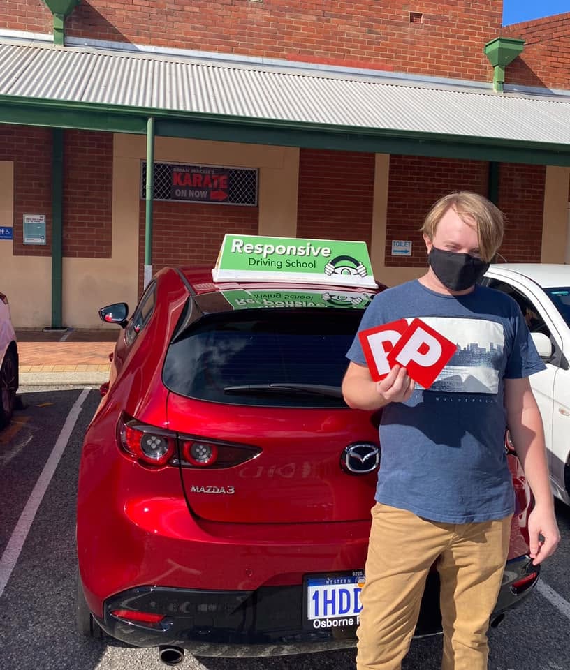 Young man in a mask holding two red P plates beside a red Mazda3 with a Responsive roof sign
