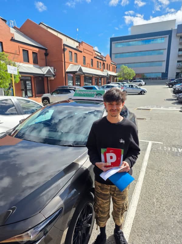Young man in a black sweatshirt holding a red P plate and a blue folder beside a dark car with a Responsive roof sign