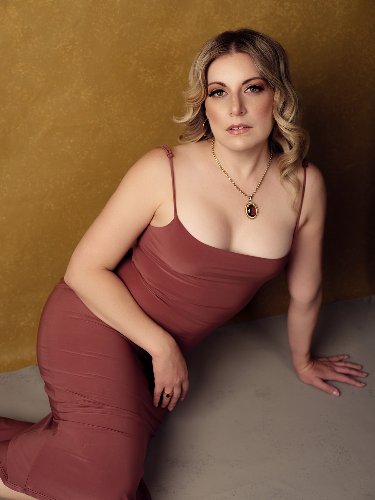Portrait of a woman in a mauve dress against a gold backdrop by Elisa Mitchell Studios